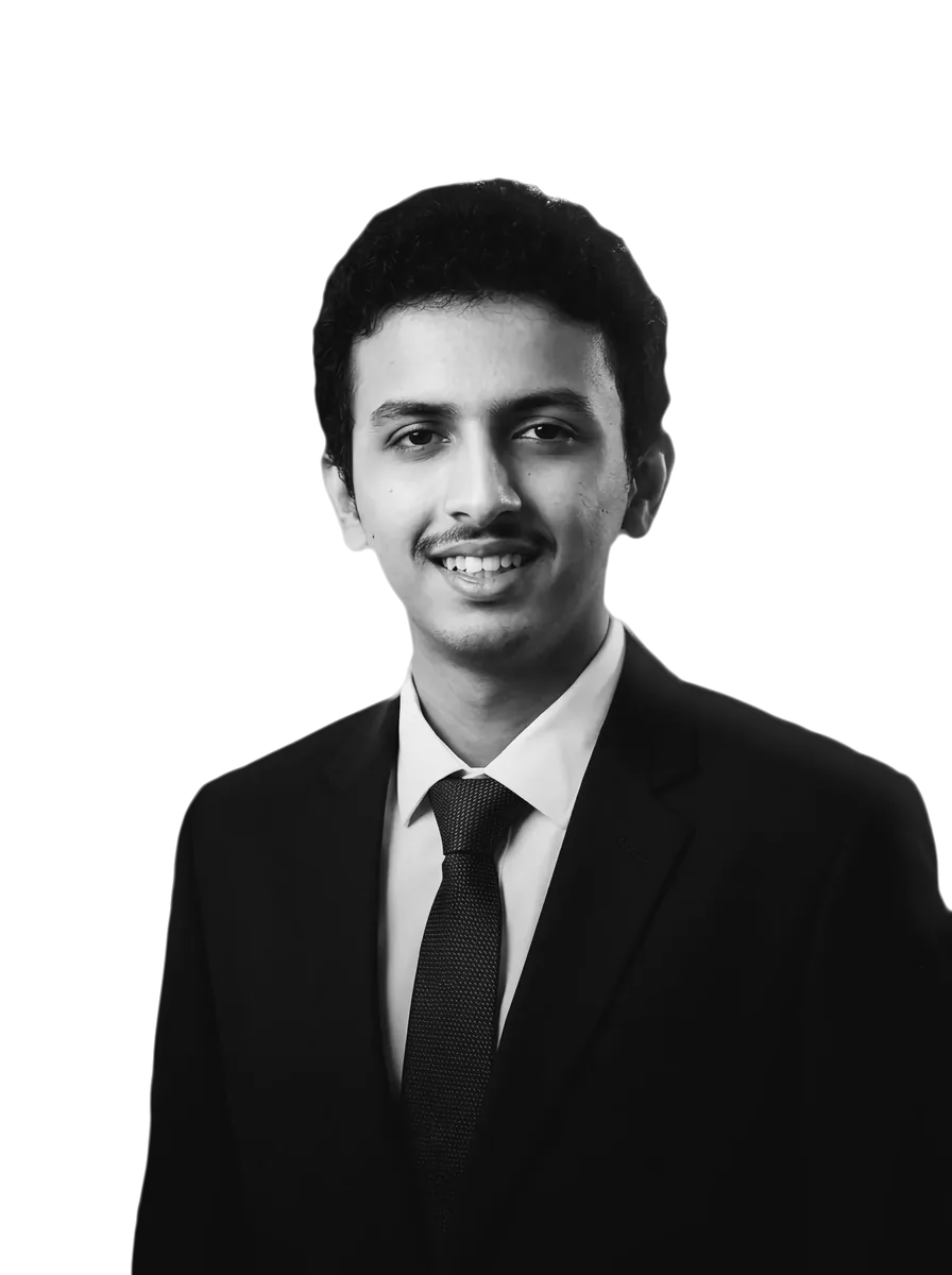 Shravan P Jois in a dark suit, white shirt and tie, smiling at the camera; black and white, on a cobalt panel.